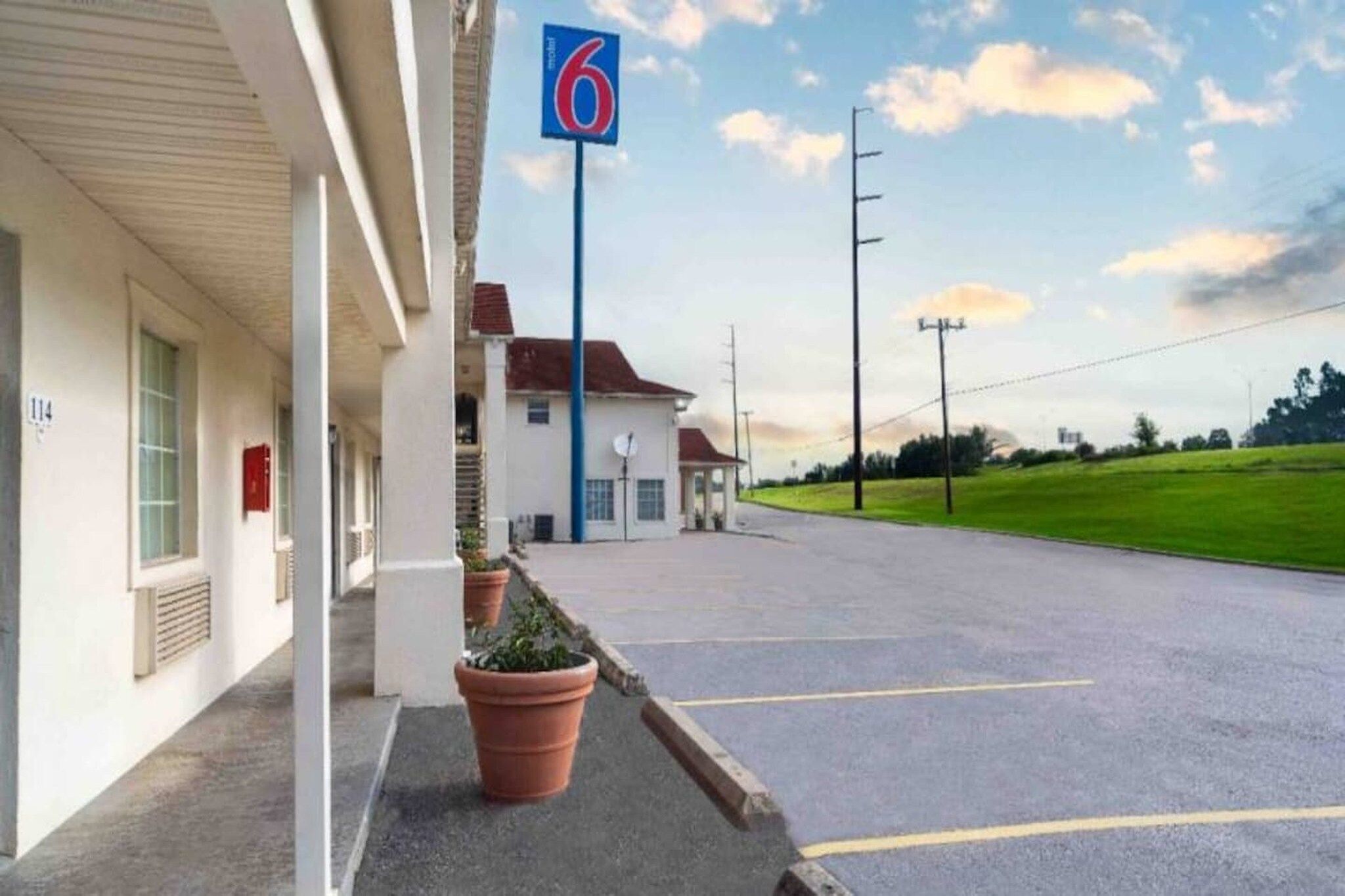 A motel with a parking lot, a building with a number '114' sign, and a '6' sign indicating the motel number.