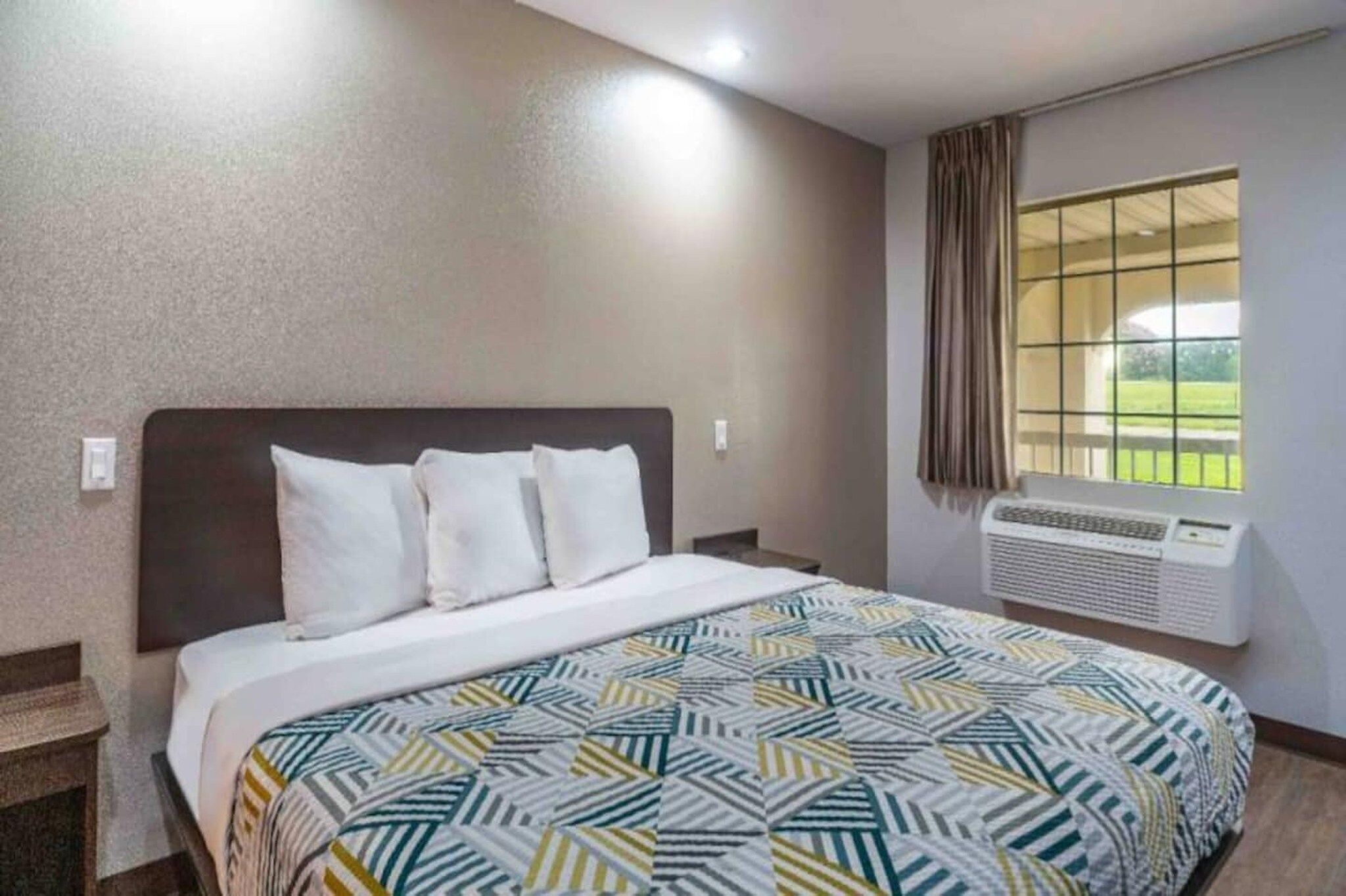 Een hotelkamer met een bed, een raam met gordijnen en een airconditioner.