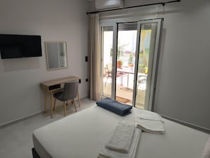 A hotel room with a bed, a desk, a chair, a TV, and a sliding glass door leading to an outdoor area. - Nidri Zone (Lefkada)