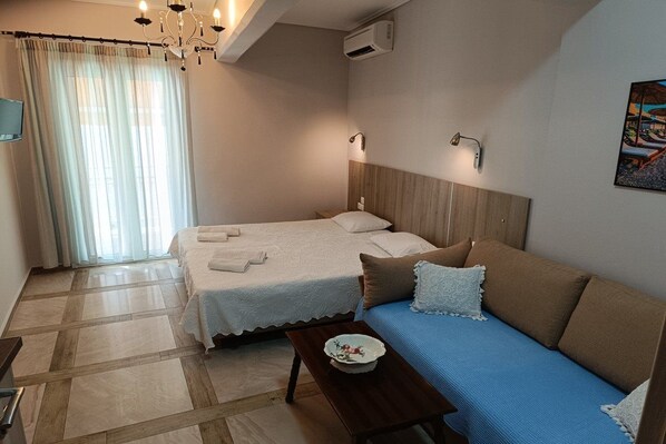 A hotel room with a bed, a sofa, a small table, and a window with curtains. - Nidri Zone (Lefkada)