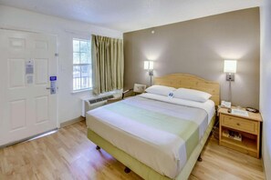 A hotel room with a bed, bedside lamps, a nightstand, a window with curtains, and a door. - 1 Queen Bed | Micfridge, Smoking (Houston)