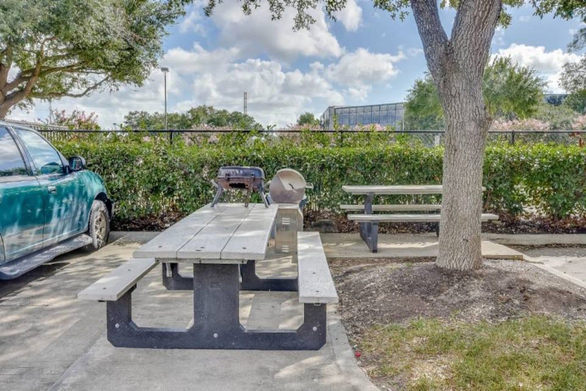 Une table de pique-nique avec des bancs, une voiture et un arbre dans un parking.
