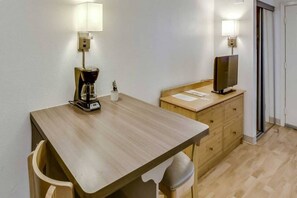Ein schlichter, kleiner Raum mit einem Holztisch, einer Kaffeemaschine, einem Fernseher auf einem Holzschrank und zwei Stühlen.