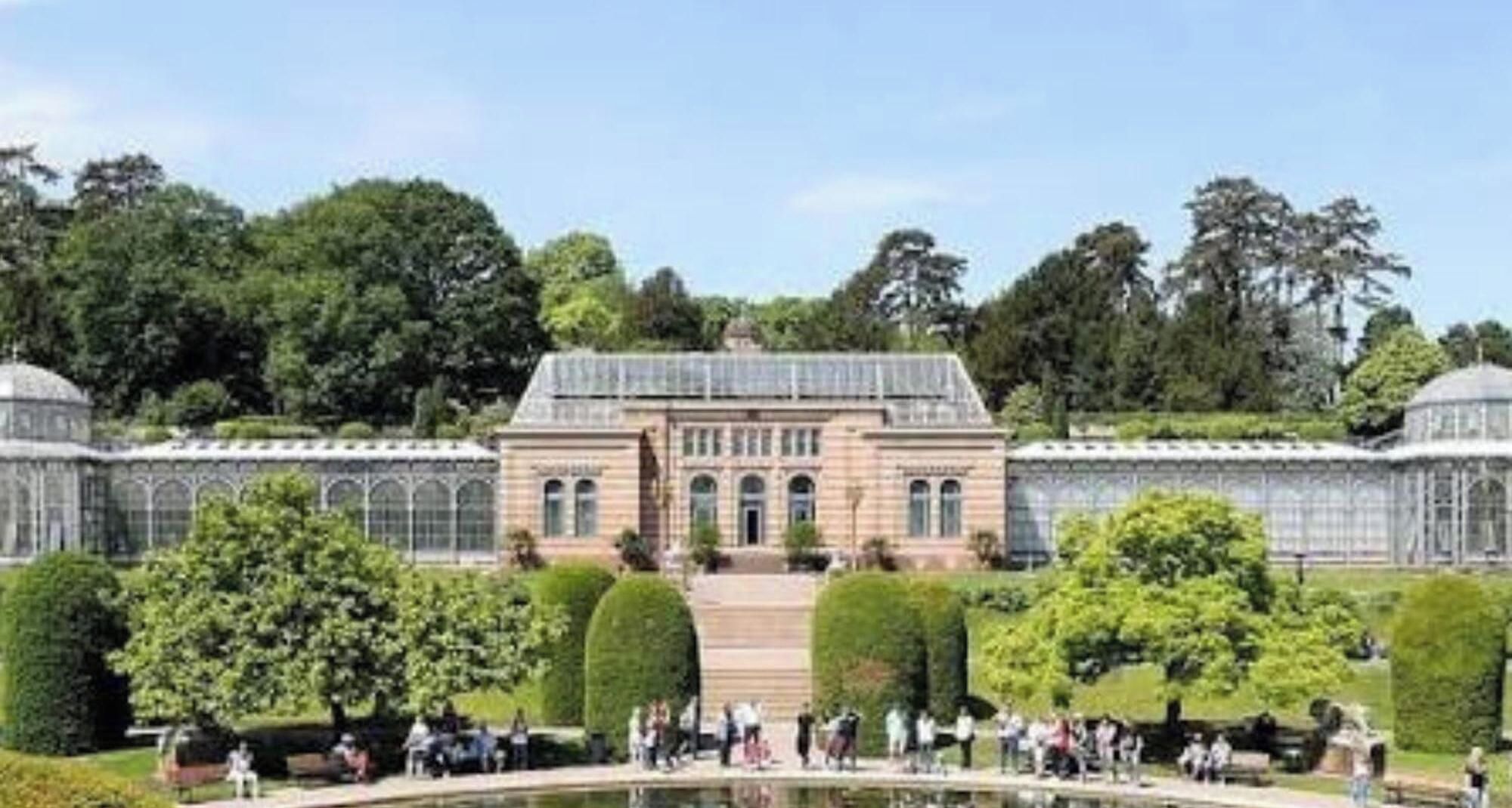 En stor bygning med en symmetrisk facade, omgivet af velplejede haver og et centralt vandelement.