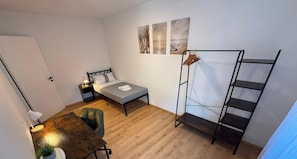 A compact room with a bed, a desk, a chair, and a wall-mounted shelf unit. - Apartment 'Elodi-living  Fellbach' with Mountain View, Balcony and Wi-Fi (Fellbach)