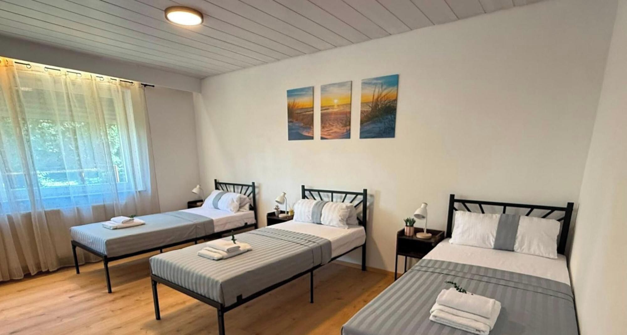Ein Hotelzimmer mit zwei Einzelbetten, einem großen Fenster mit Vorhängen und drei Bildern an der Wand.