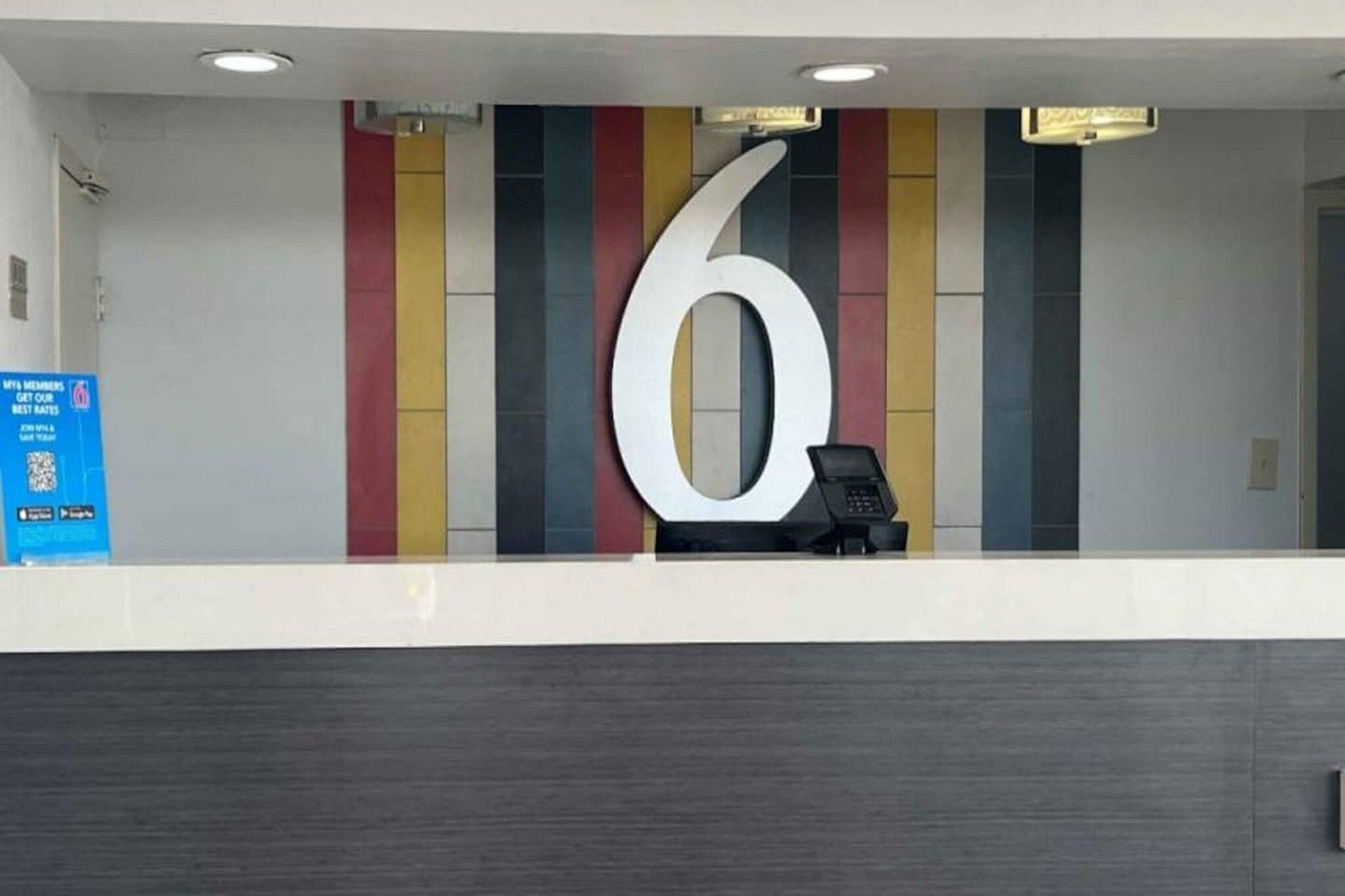 A reception desk with a large number '6' on the wall, a phone, and a blue informational sign.