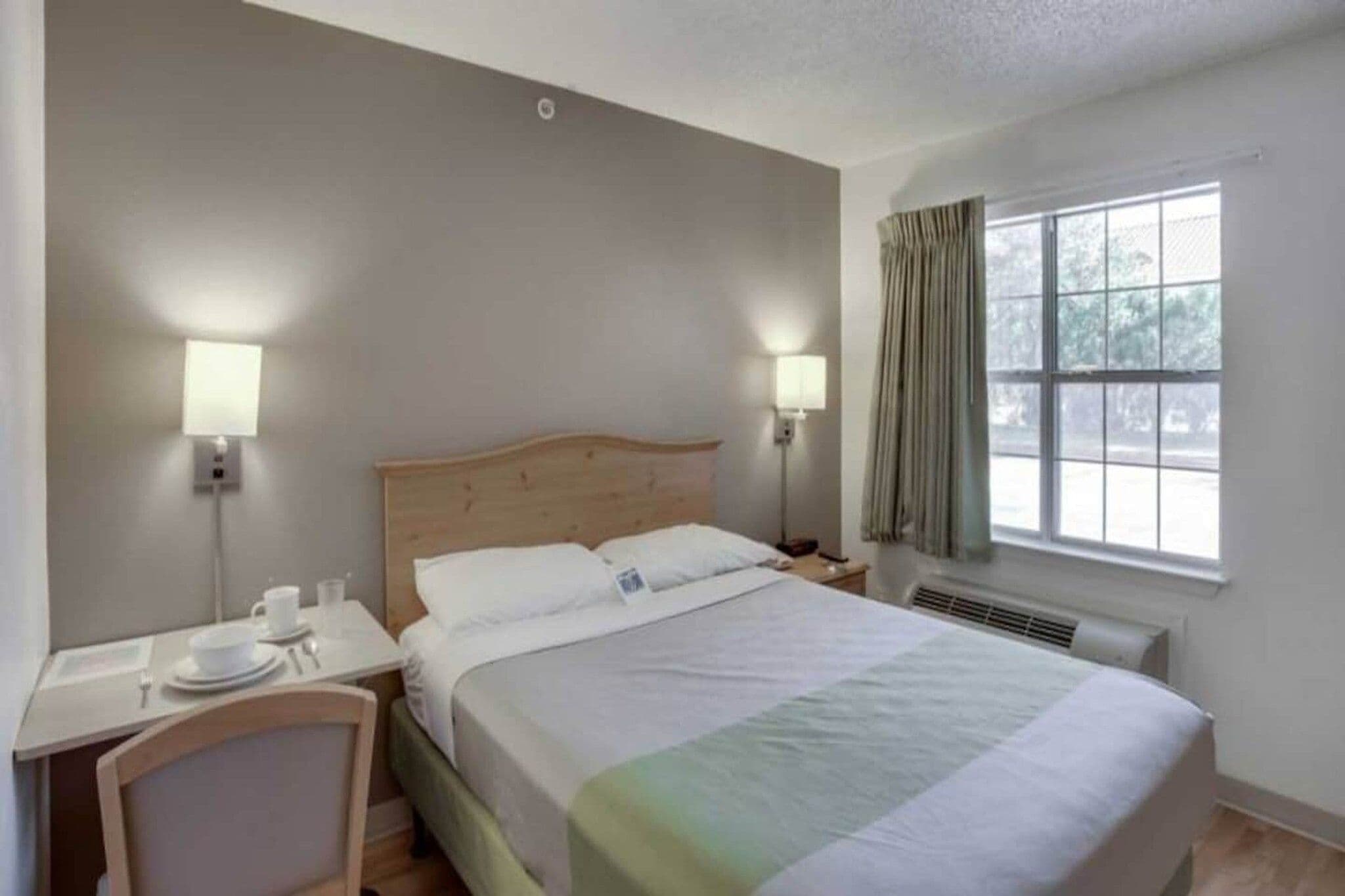 Ett hotellrum med en säng, sängbord, lampor, ett fönster med gardiner och ett element.