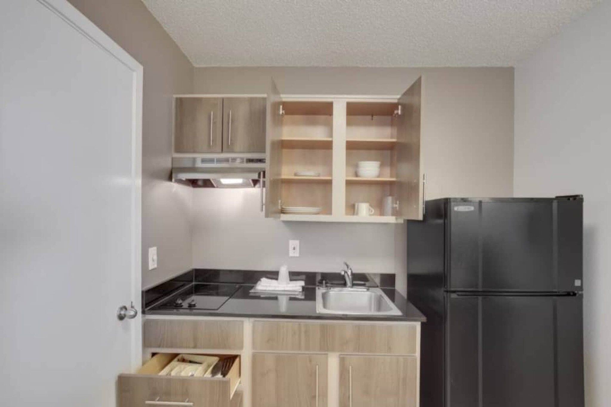 A compact kitchen with a black refrigerator, a built-in oven, and wooden cabinets.