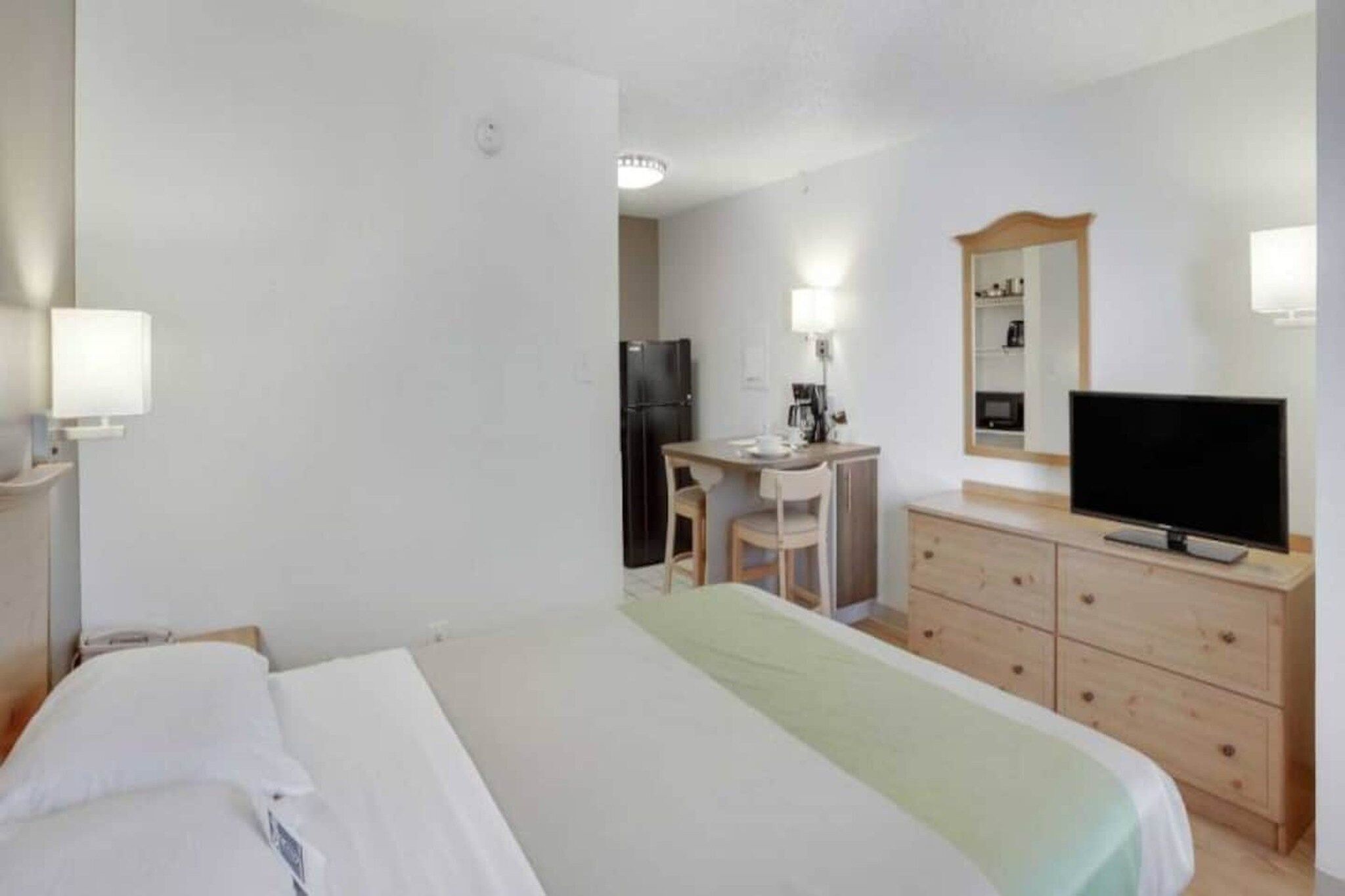 A hotel room with a bed, a desk, a chair, a television, and a dresser.