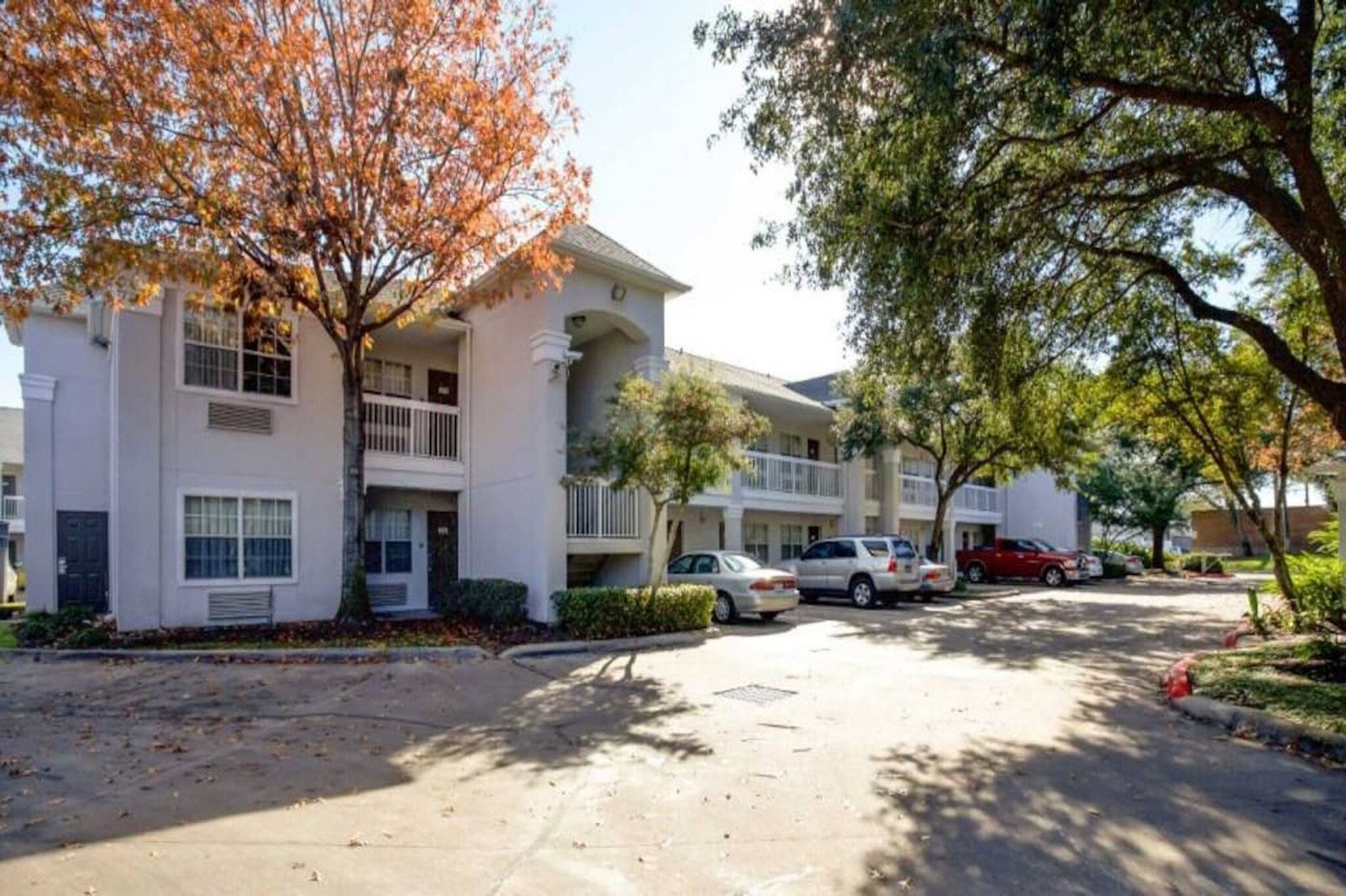 A multi-story residential building with a central courtyard, parking spaces, and mature trees.