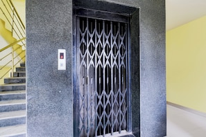 A metal gate with a digital display, a staircase with yellow handrails, and a textured wall. - Hotel O LB Nagar Metro Station (Hyderabad)