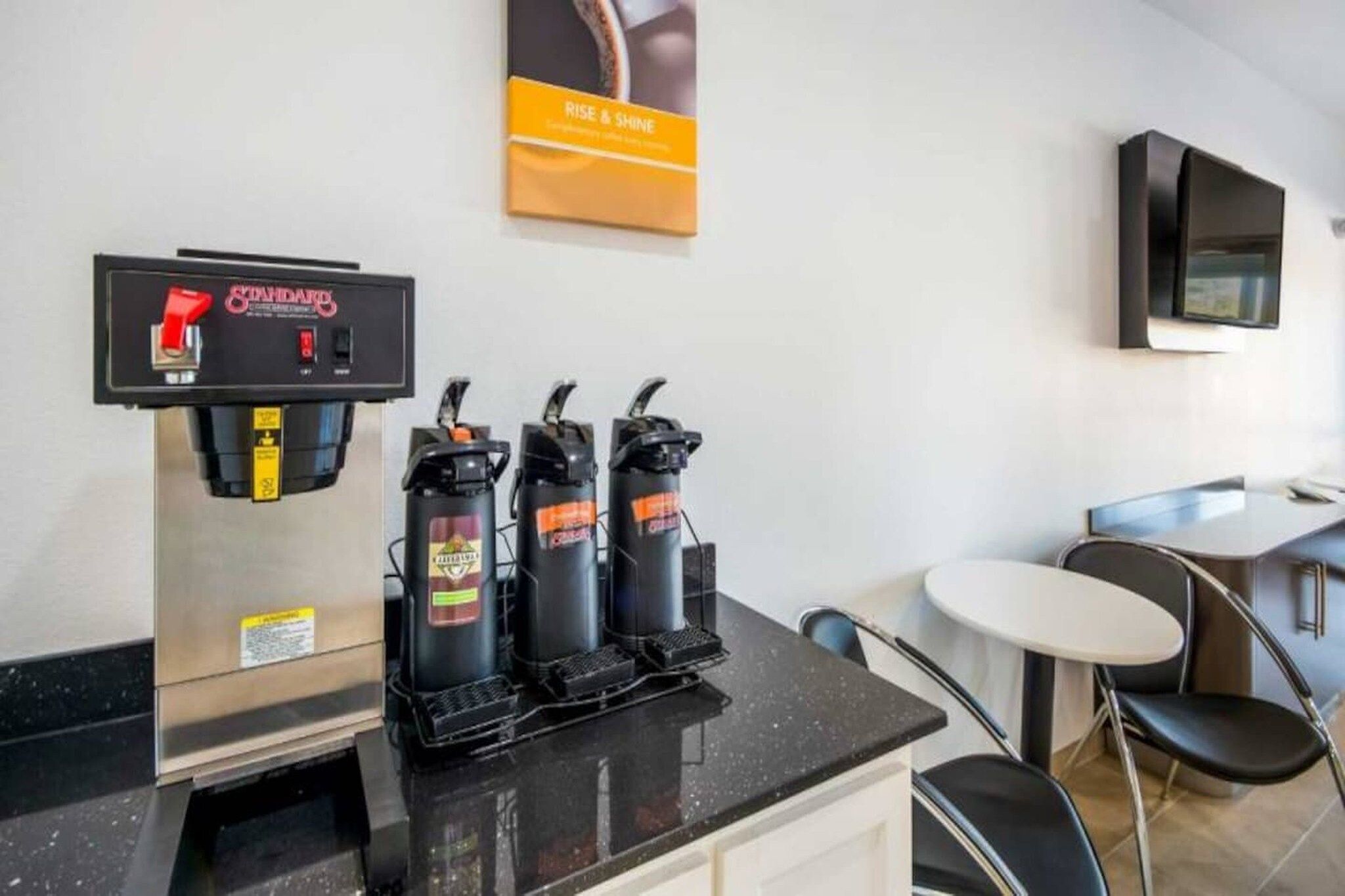 A coffee machine, two espresso machines, a TV, and a small table with chairs in a modern room.