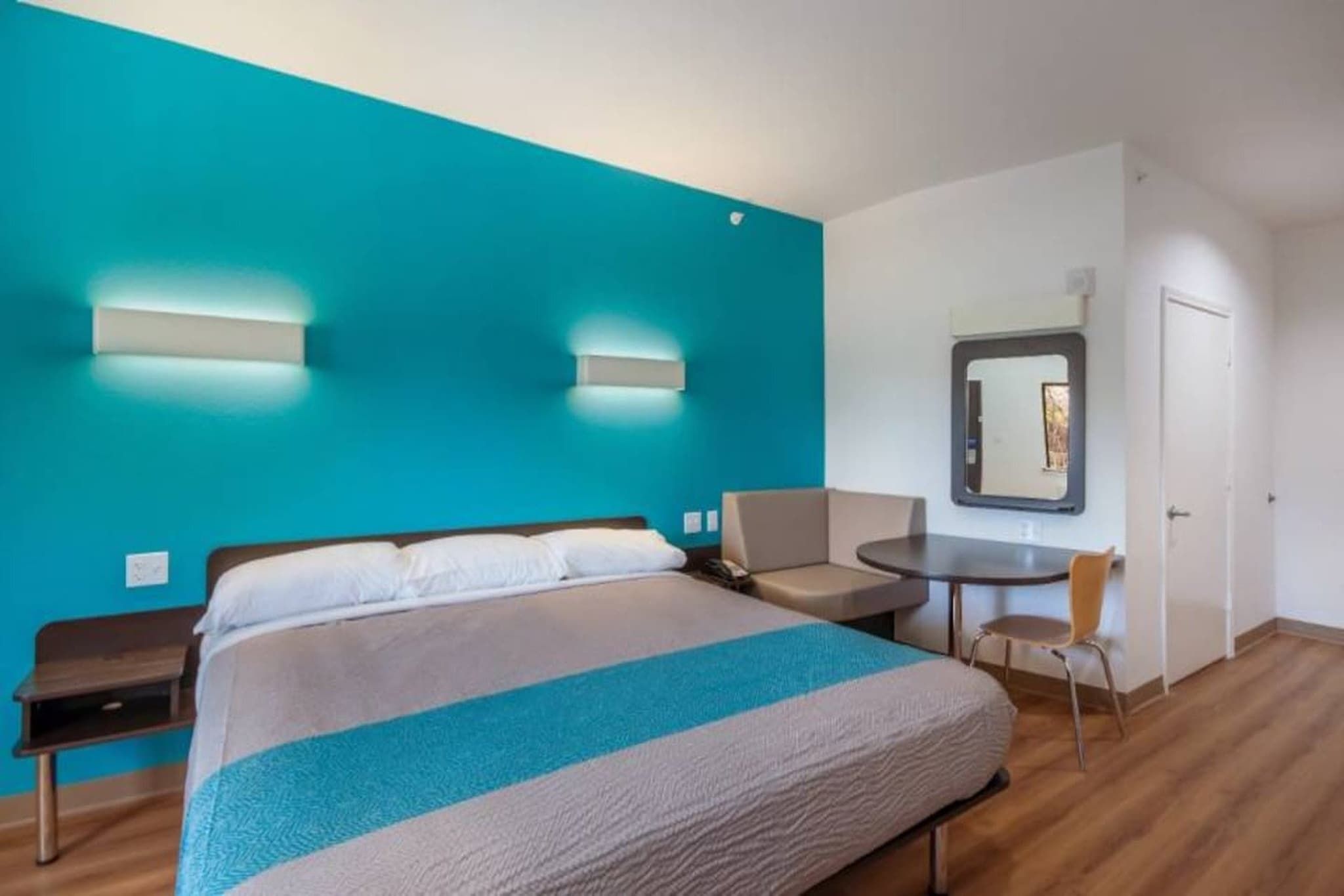 A hotel room with a large bed, a desk, a chair, and a mirror.