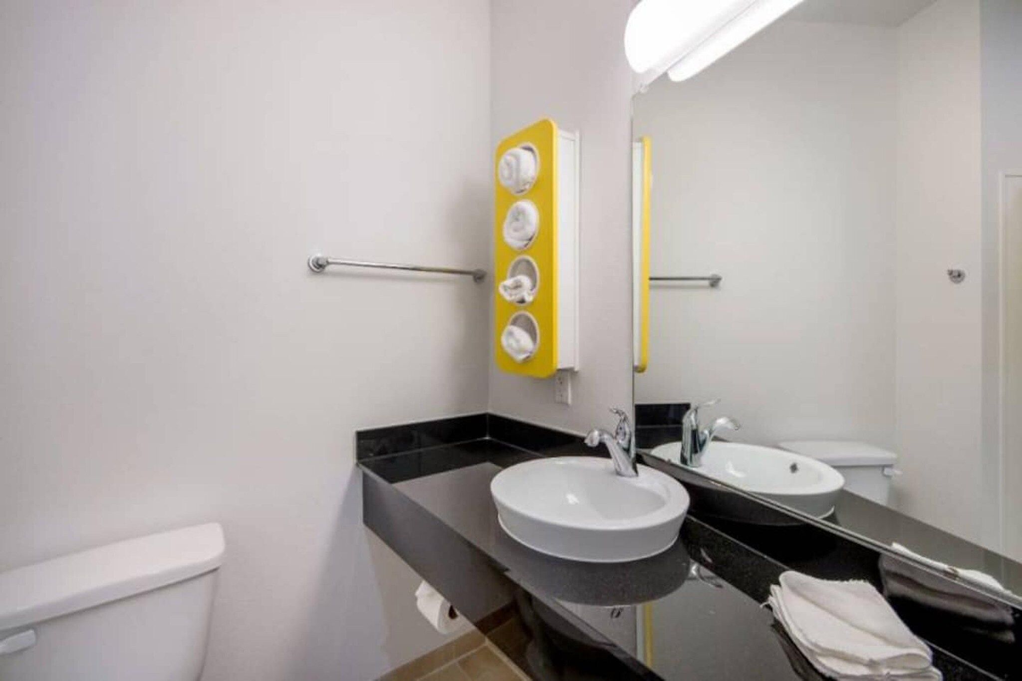 A modern bathroom with two sinks, a toilet, and a mirror with a yellow towel holder.
