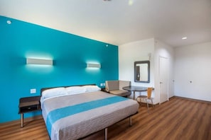 Ein Hotelzimmer mit Bett, Schreibtisch, Stuhl, Spiegel und Tür.