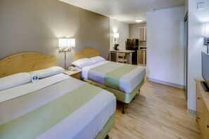 Quarto de hotel com duas camas, uma mesa, uma cadeira, televisão e uma cozinha compacta.