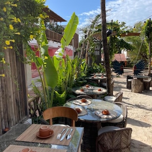 Een terras met ronde tafels, stoelen en een tropische tuin.