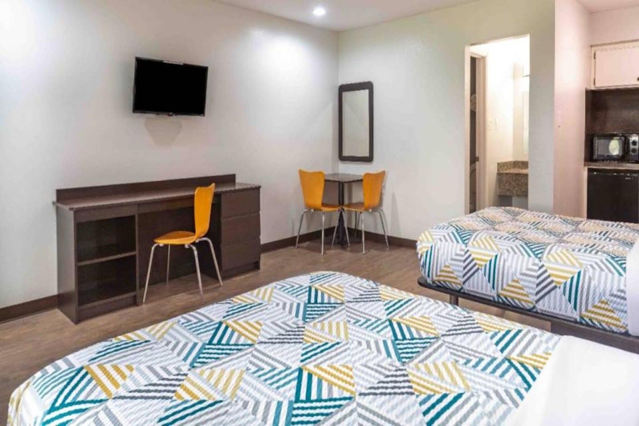 Habitación de hotel con escritorio, dos sillas, cama con ropa de cama estampada, televisor y espejo.