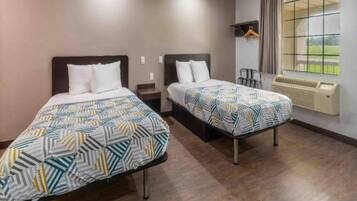 Habitación de hotel con dos camas, una ventana con cortinas, un calentador y un perchero.