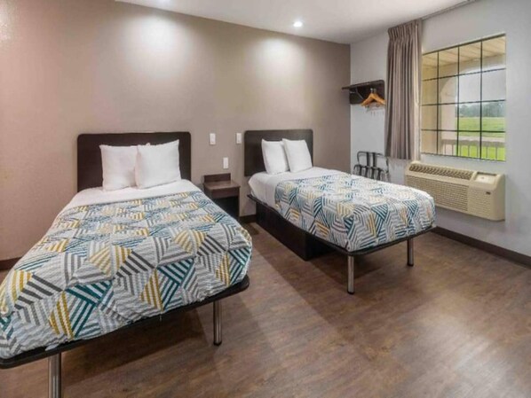 A hotel room with two beds, a window with curtains, a heater, and a coat rack.