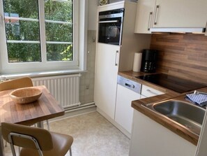 Eine kompakte Küche mit Einbauofen, Geschirrspüler und Spüle. Ein Fenster sorgt für natürliches Licht und bietet einen Blick ins Grüne.