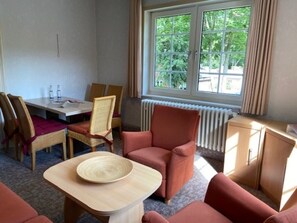 Ein Zimmer mit Esstisch, Stühlen, einer Couch, einem Heizkörper und einem Fenster mit Vorhängen.