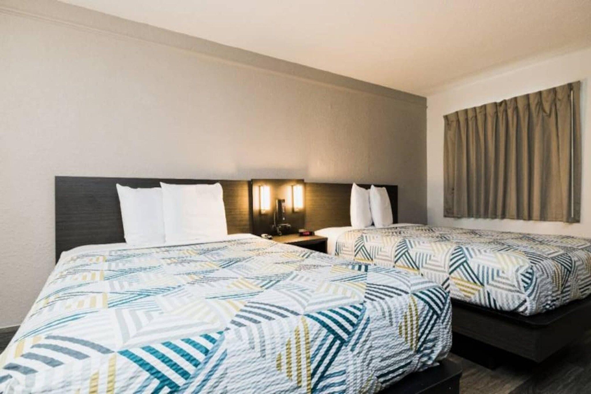 A hotel room with two beds, each with a patterned bedspread, a nightstand with a lamp, and a wall-mounted artwork.