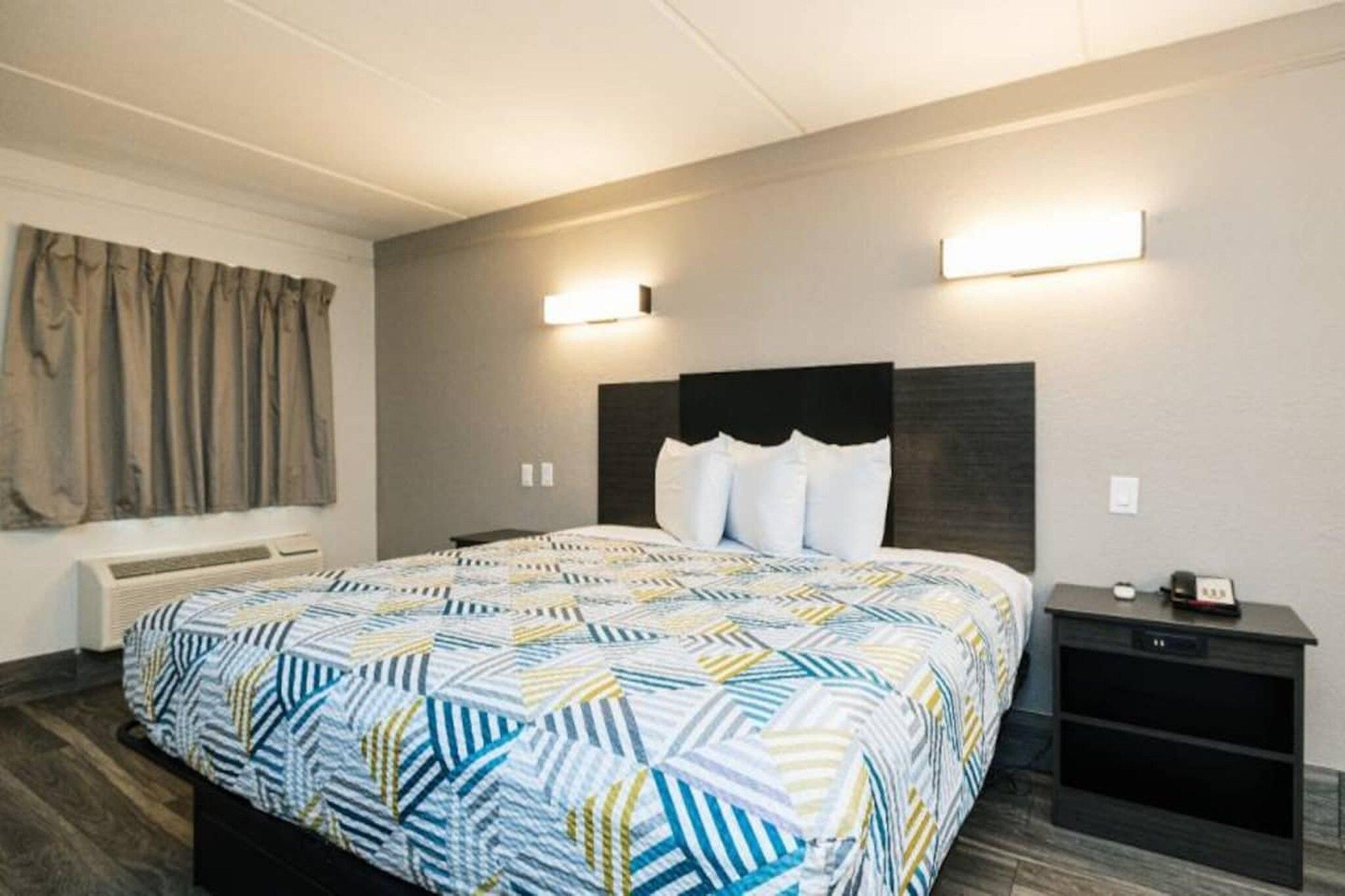 A hotel room with a large bed, a bedside table, a nightstand, and a window with curtains.