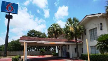 A hotel with a covered entrance, palm trees, and a clear blue sky.