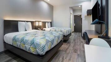 A hotel room with two beds, a desk, a chair, a TV, and a door leading to a hallway.