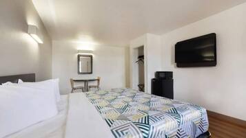 A hotel room with a bed, a desk, a chair, a television, and a coat rack.