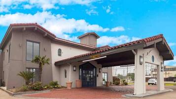 A two-story building with a red-tiled roof, a covered entrance, and a parking area.
