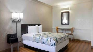 A hotel room with a bed, bedside table, lamp, chair, and a small table with a mirror.