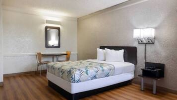 A hotel room with a bed, a desk, a chair, a nightstand, and a wall-mounted lamp.