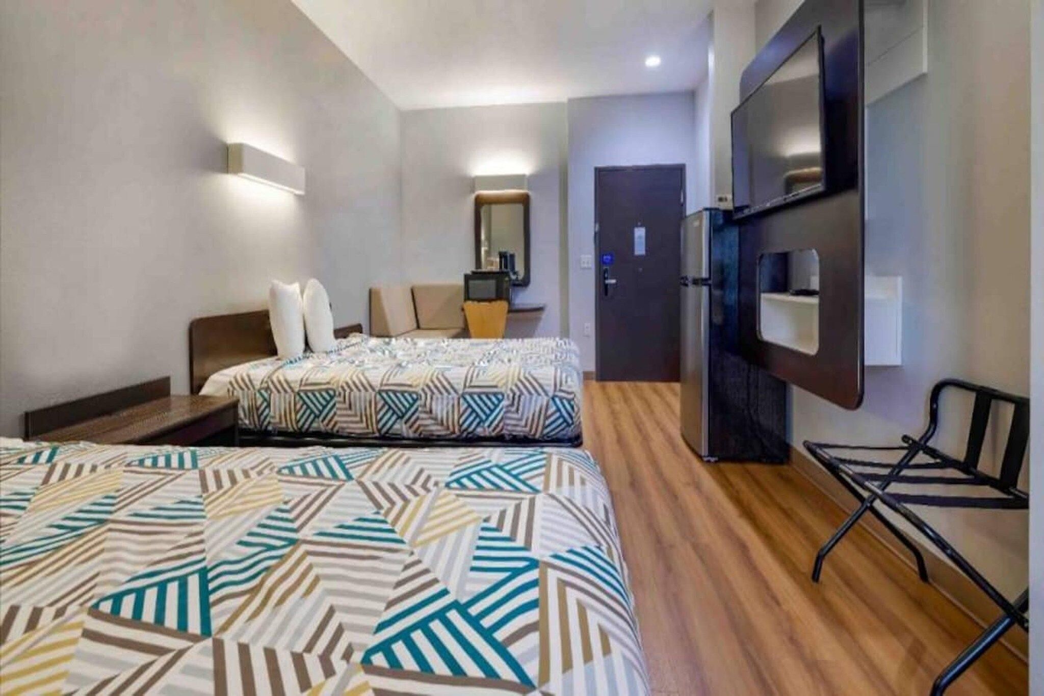 A hotel room with two beds, a desk, a chair, a TV, and a minibar.