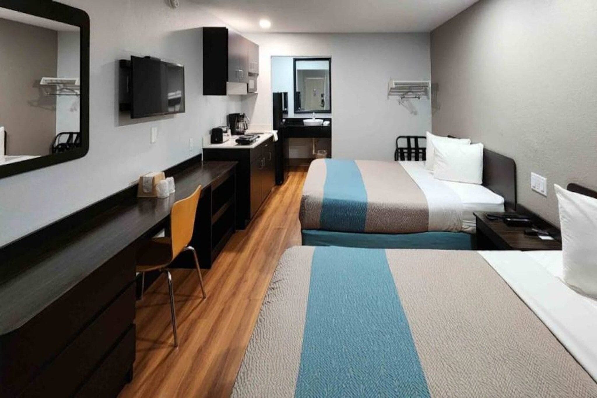 A hotel room with a bed, a desk, a chair, a mirror, a television, and a small kitchenette.