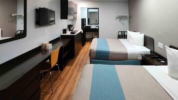 A hotel room with a bed, a desk, a chair, a mirror, a television, and a small kitchenette.