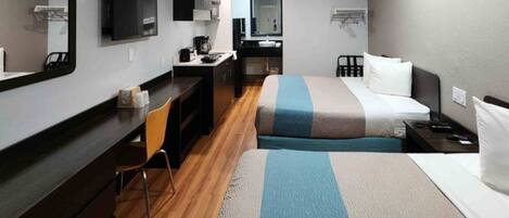 A hotel room with a bed, a desk, a chair, a mirror, a television, and a small kitchenette.