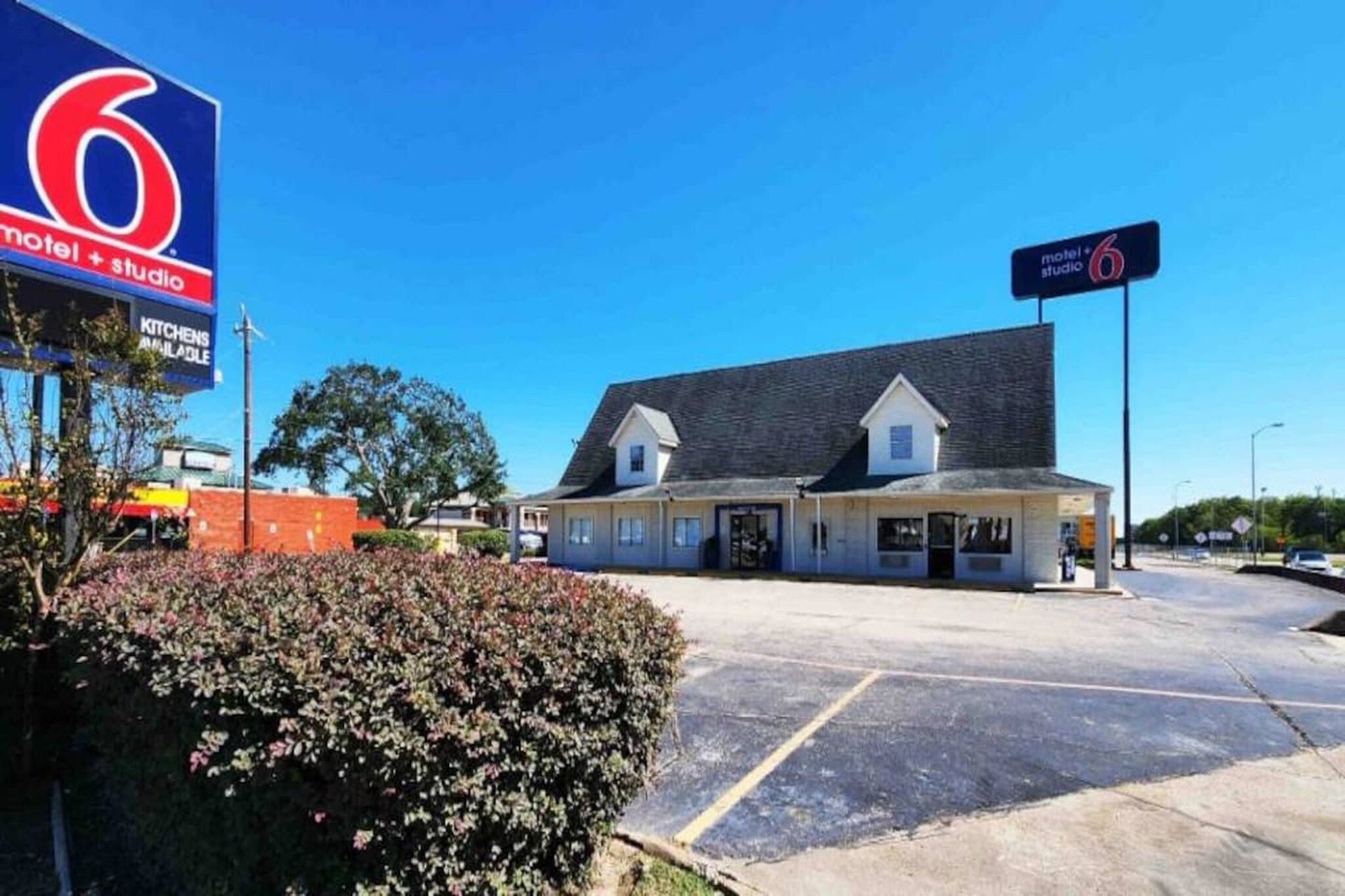 A motel with a large sign, a parking lot, and a building with a sloped roof.