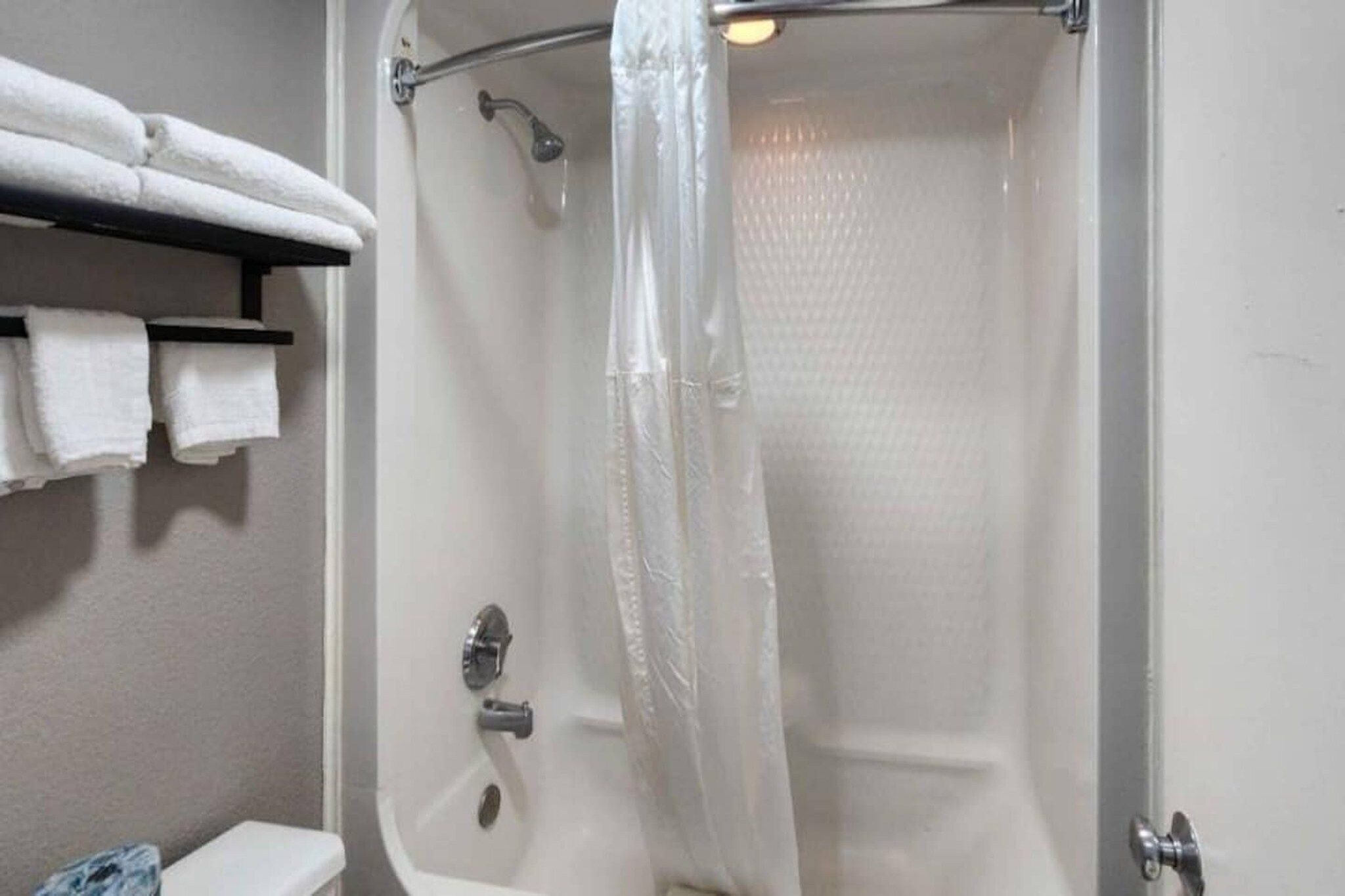 A bathroom with a shower, a toilet, and a shelf with towels.