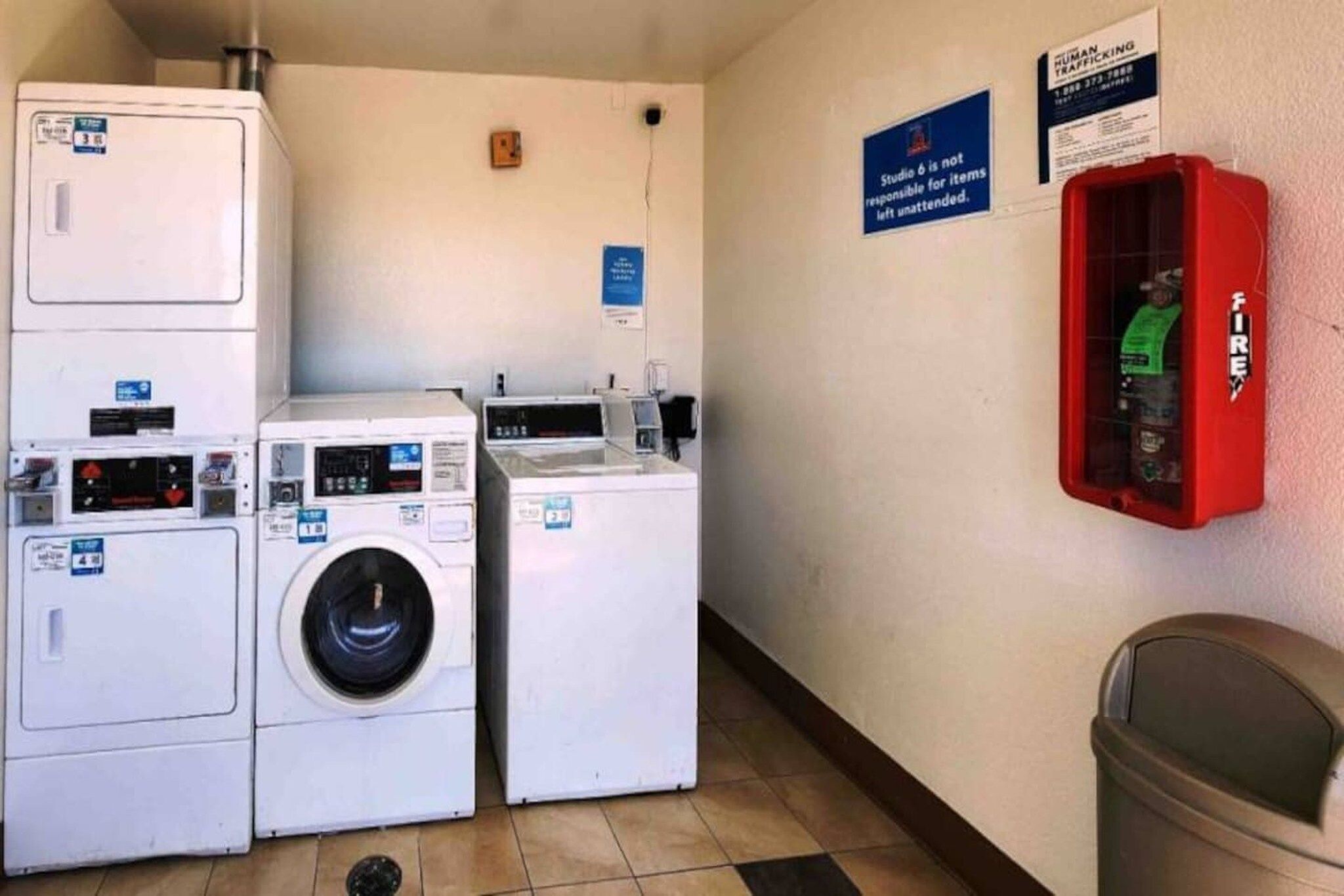 A laundry room with stacked washers and dryers, a fire extinguisher, and a sign indicating unattended items are not the responsibility of Studio 6.