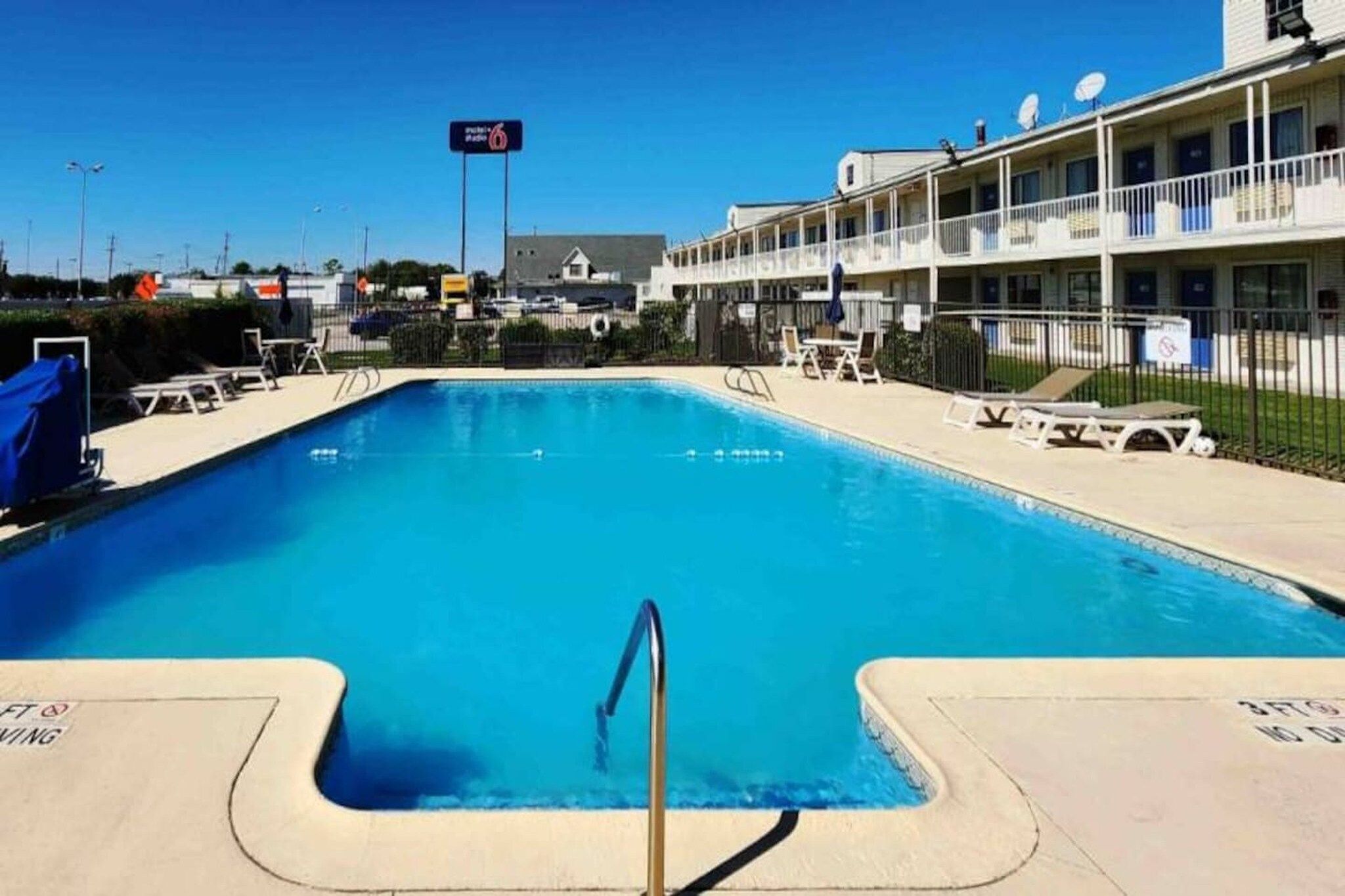 A swimming pool with a metal ladder, lounge chairs, and a building with balconies in the background.