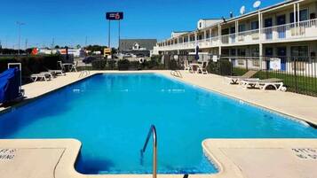 A swimming pool with a metal ladder, lounge chairs, and a building with balconies in the background.