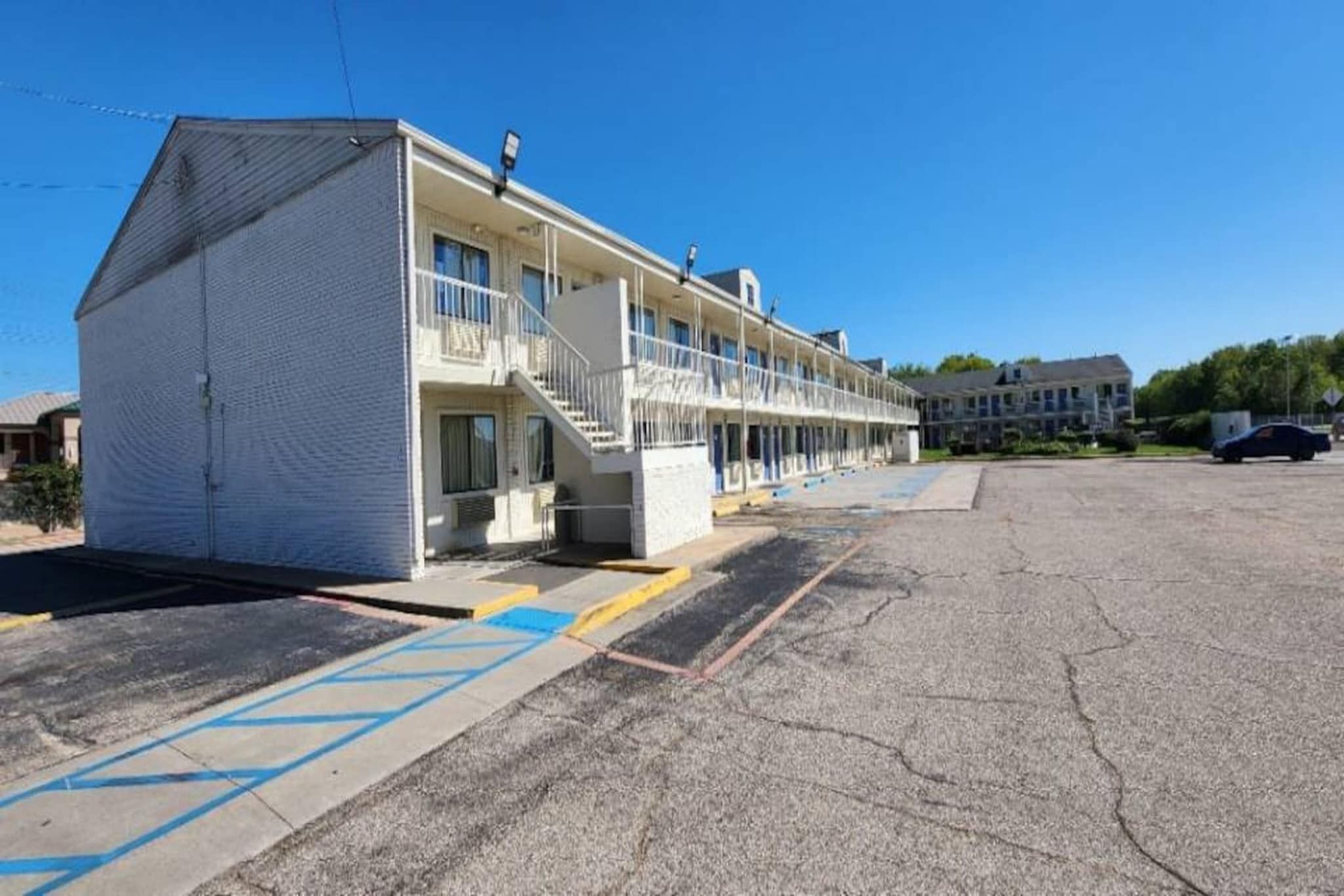 A motel with a two-story structure, a covered parking area, and a clear sky.