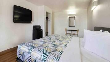 A hotel room with a bed, a flat-screen TV mounted on the wall, a desk with a chair, and a mirror.