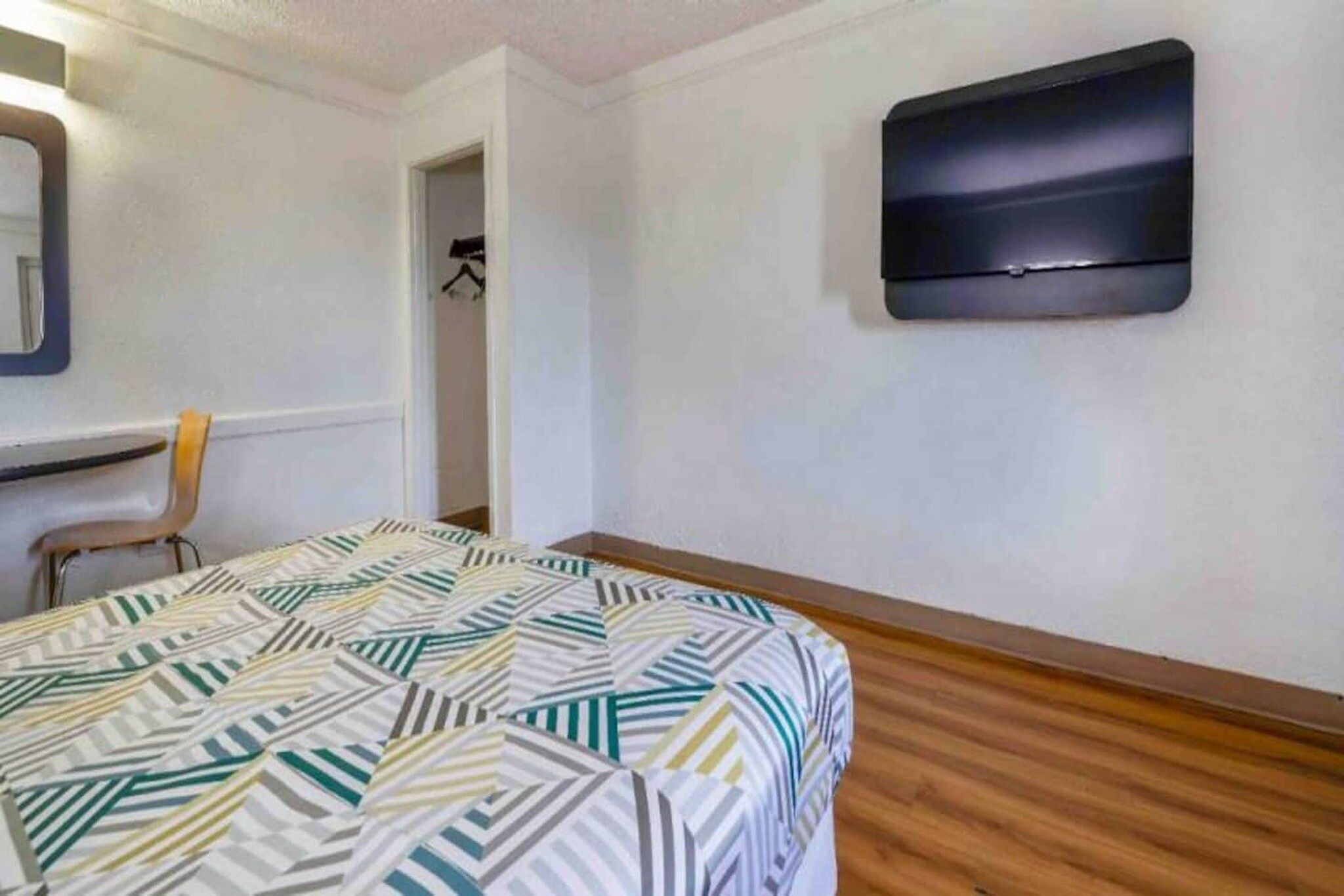 A room with a bed, a chair, a coat rack, and a wall-mounted TV.