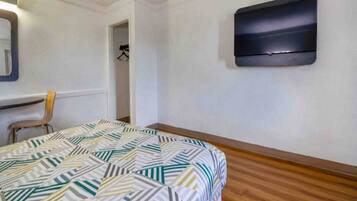 A room with a bed, a chair, a coat rack, and a wall-mounted TV.