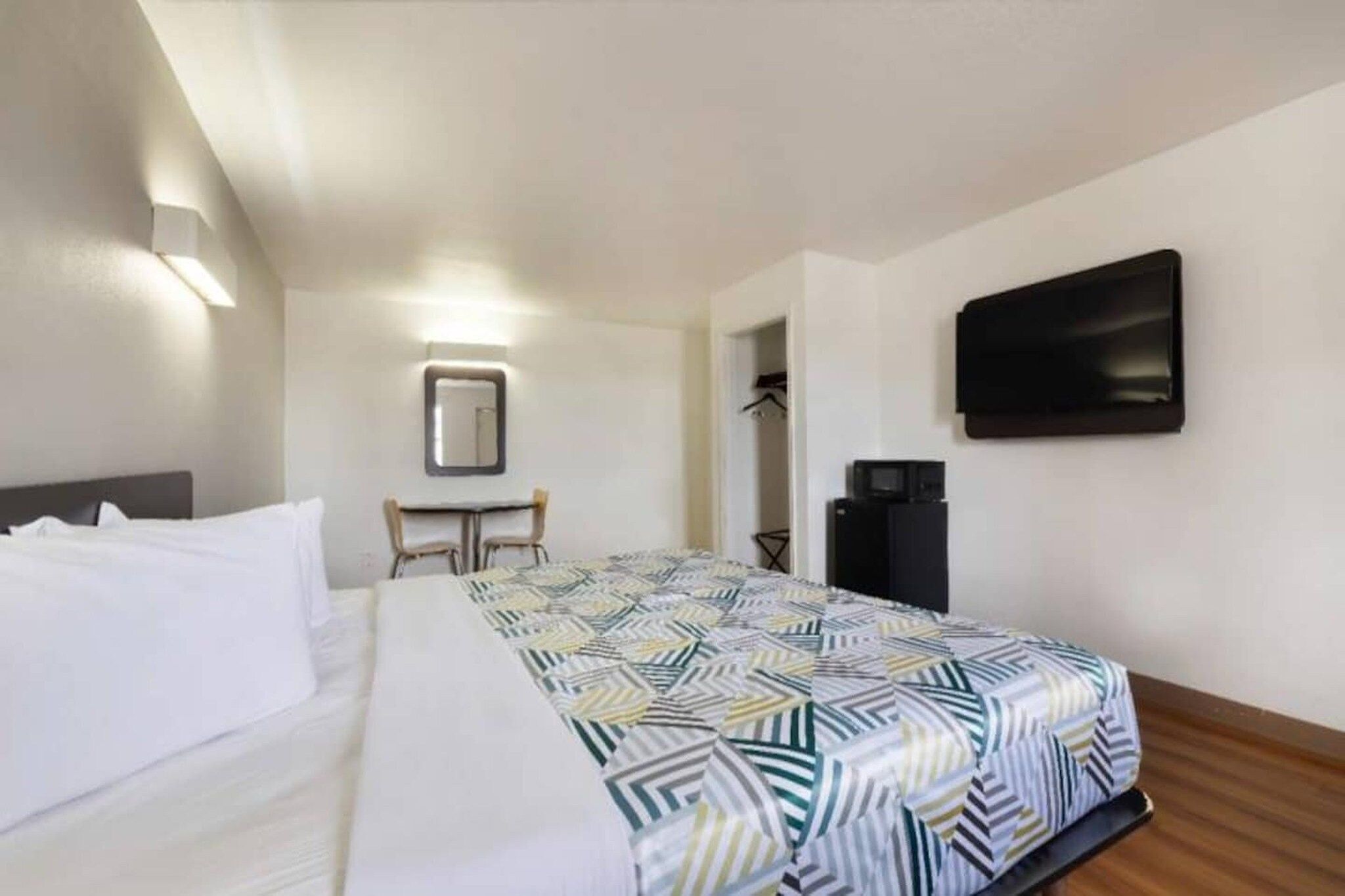 A hotel room with a bed, a desk, a chair, a television, and a coat rack.