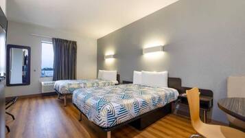 A hotel room with two beds, a small table, a chair, and a window with curtains.